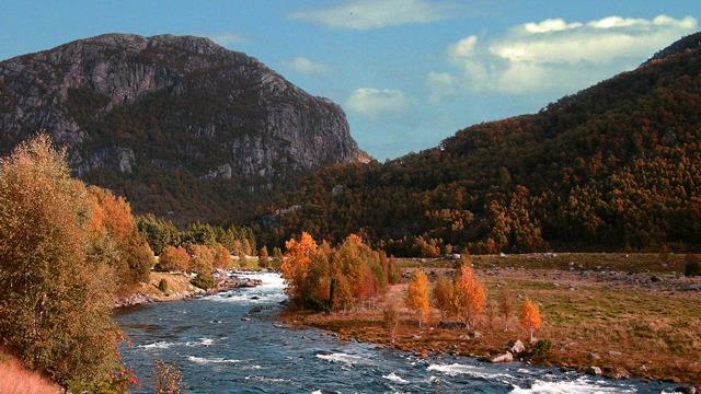 En vakker elv som renner gjennom et høstlandskap med fargerike trær og fjell i bakgrunnen.