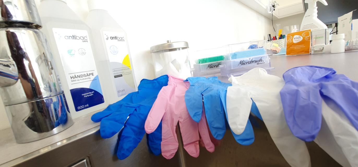 Fargerike hansker og rengjøringsmidler på et bord i et laboratorium.