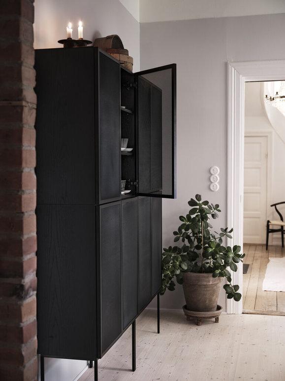 Moderne svart skap med glassdører i en lys gang, med en potteplante ved siden av.