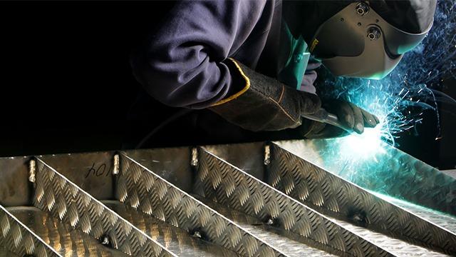 En sveiser arbeider med metallplater, og det spruter gnister fra sveiseprosessen.