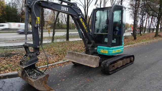Gravemaskin parkert langs veien med høstløv rundt, klar for graving og anleggsarbeid.