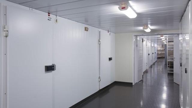 Lys korridor med hvite oppbevaringsrom og grått gulv i et moderne lageranlegg.