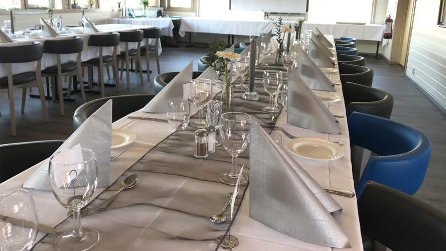Langbord dekket med sølvfargede servietter og glass i en restaurant med moderne interiør.