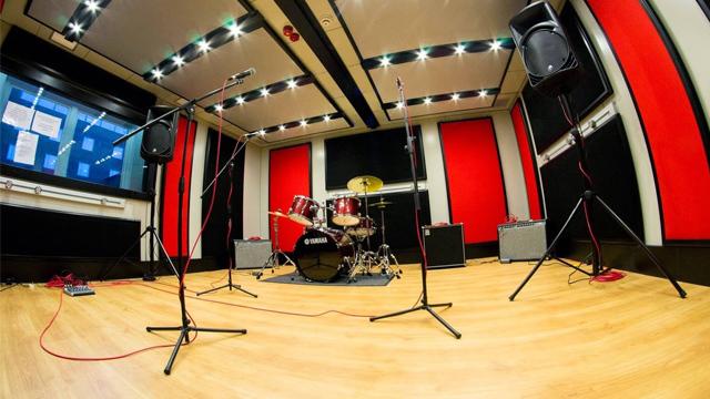 Et musikkstudio med trommesett, mikrofoner og høyttalere, med røde vegger og tregulv.