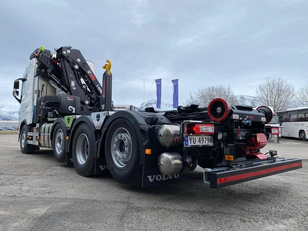 En svart Volvo lastebil med kran, parkert på en grusvei med trær i bakgrunnen.