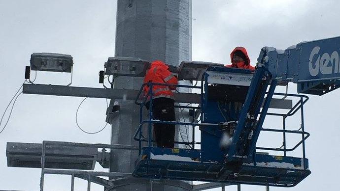 To personer i oransje jakker arbeider på en heis ved en stolheis i snøvær.
