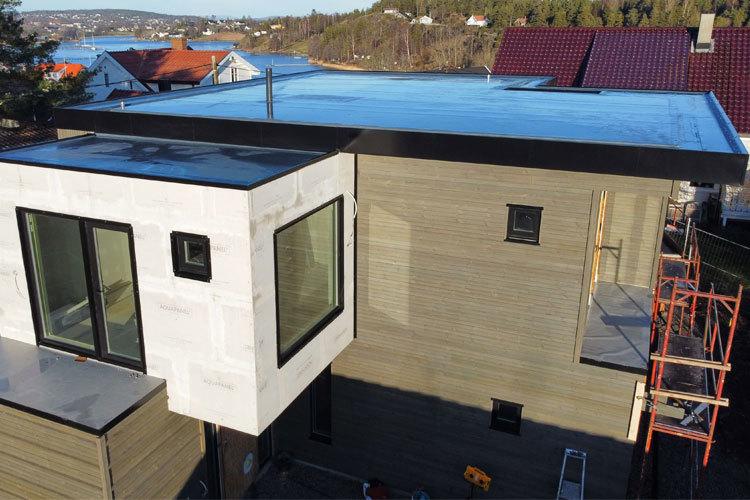 Moderne hus med flat tak og store vinduer, bygget i et boligområde ved sjøen.