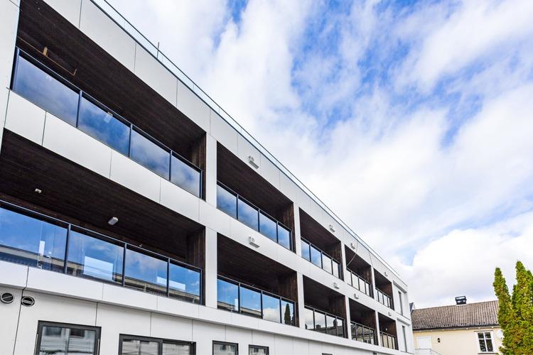 Moderne bygning med store vinduer og balkonger under en blå himmel med skyer.
