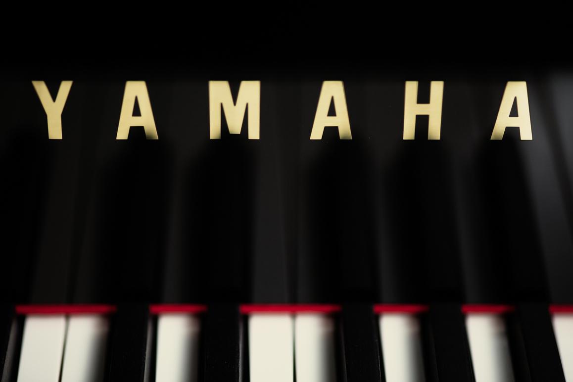 Nærbilde av et Yamaha piano med svarte og hvite tangenter og navnet "Yamaha" i gullbokstaver.