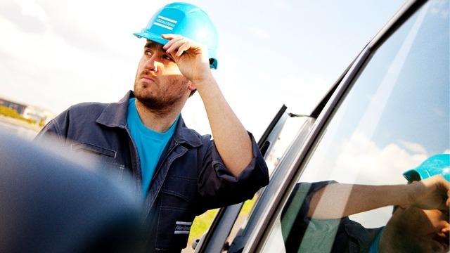 En mann i blå hjelm står ved siden av en bil og ser ut mot horisonten. Han har på seg arbeidsklær.