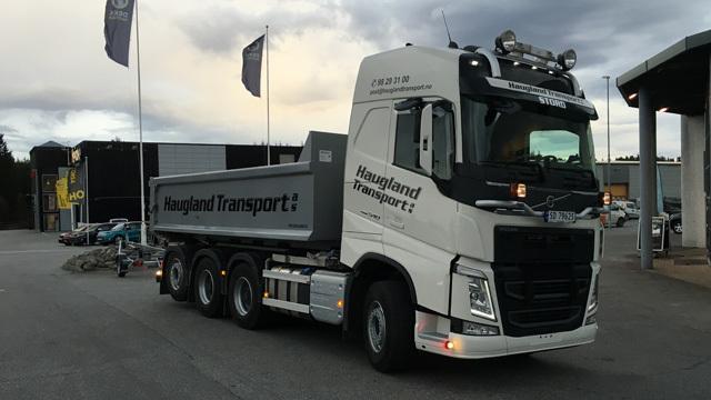 En lastebil fra Haugland Transport med tilhenger, parkert foran en bygning under en skyet himmel.