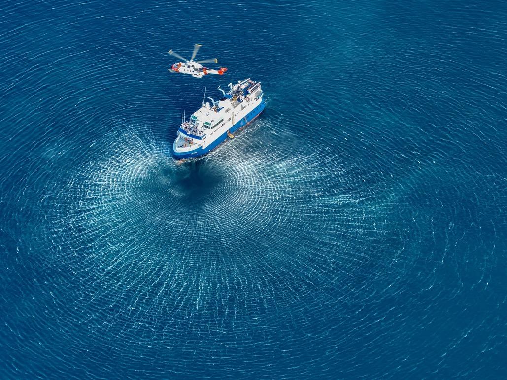 Et forskningsskip med en helikopter over vannet, som skaper sirkler i det blå havet.