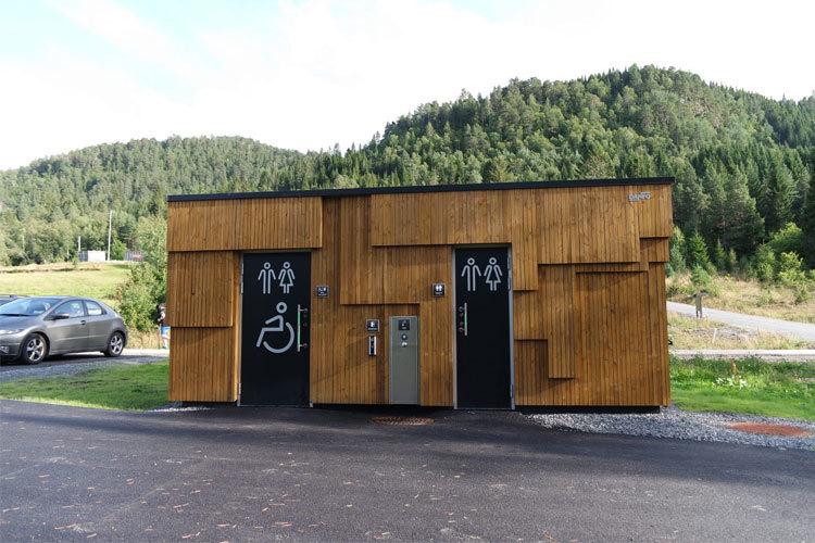 Toalettbygning i tre med universell utforming, plassert i naturskjønne omgivelser med fjell i bakgrunnen.