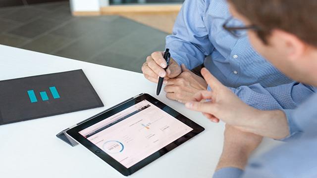 To personer som diskuterer data på en nettbrett, med grafer og diagrammer synlige på skjermen.