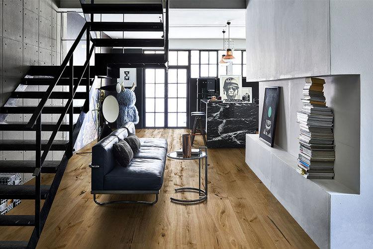 Moderne stue med svart sofa, glassbord, trapp i metall og store vinduer som slipper inn naturlig lys.
