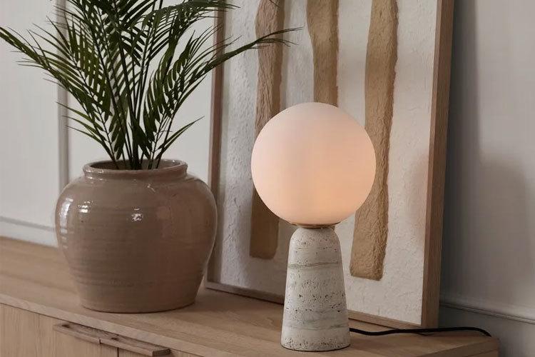 En moderne lampe med en rund, lysende globus står på et bord ved siden av en dekorativ plante og en vase.