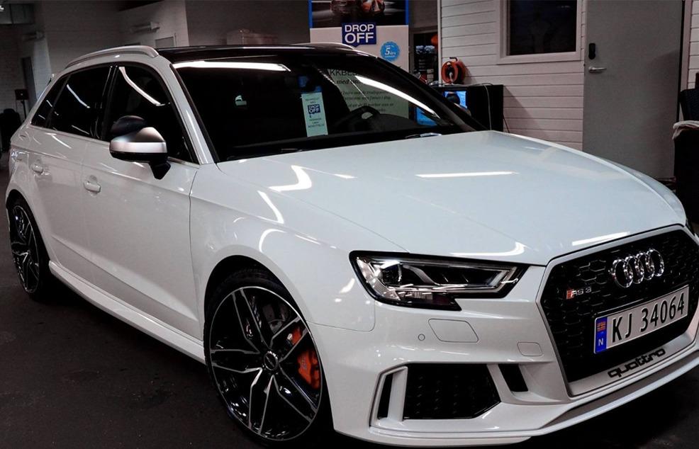 En hvit Audi RS3 med sorte detaljer og sportslige felger, parkert i en bilutstilling.