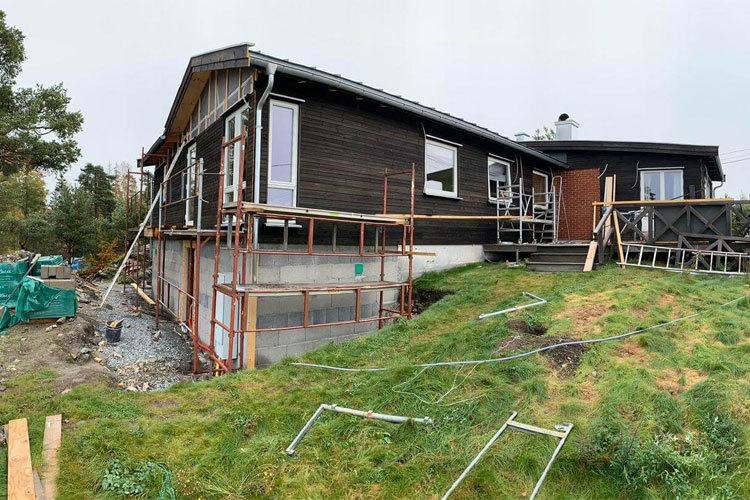 Hus under oppussing med stillas, gressplen og trær i bakgrunnen.