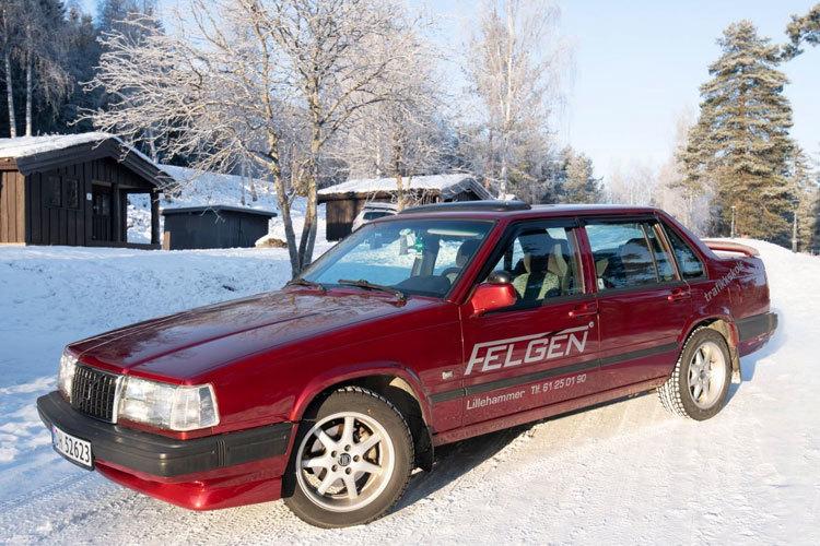 En rød bil parkert på en snødekt vei med hytter i bakgrunnen.