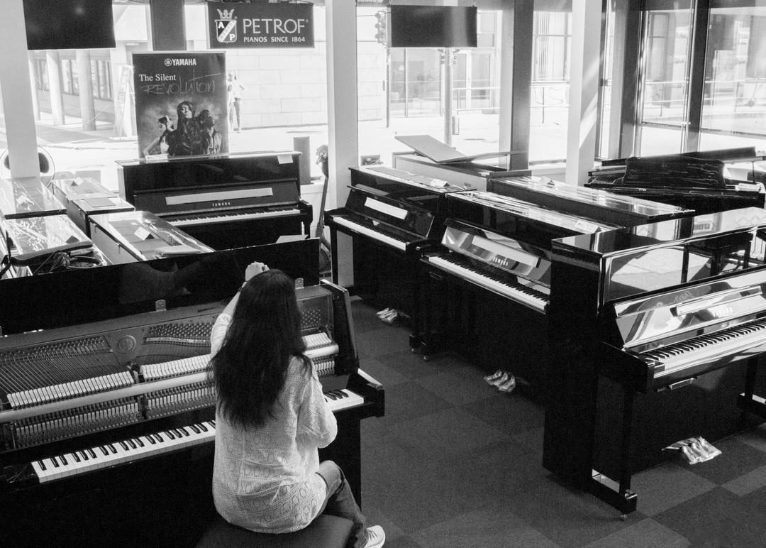 En kvinne spiller piano i en musikkbutikk med flere pianoer rundt seg.