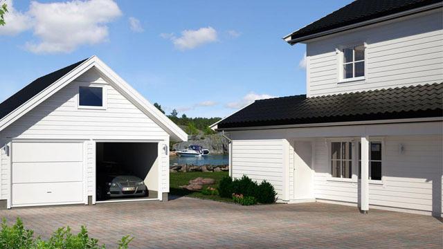 Moderne hus med garasje og bil, beliggende ved vannet med båter i bakgrunnen. Klar blå himmel.