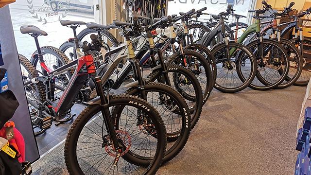 En rekke sykler i en butikk, inkludert elektriske og mountainbikes, med fokus på detaljer og variasjon.