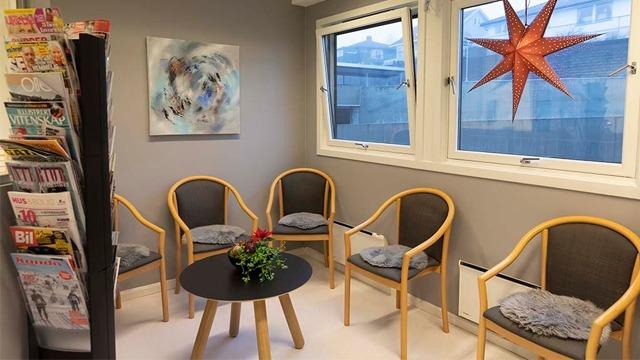 Moderne venterom med stoler, bord, planter og magasiner, dekorert med en rød stjerne i vinduet.