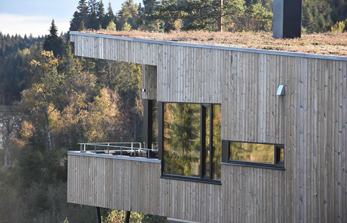 Moderne hus med trepanel og stor vindu, beliggende i skogkledd område med utsikt over naturen.