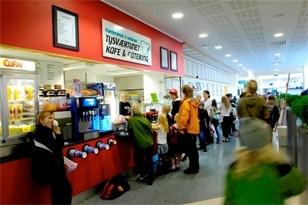 Kafé med folk som står i kø, mat og drikke tilgjengelig, fargerik innredning og koselig atmosfære.