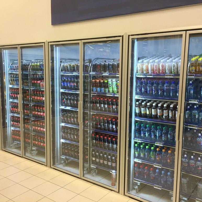 Kjøleskap med forskjellige brusflasker og bokser i en butikk, med lys som fremhever utvalget.