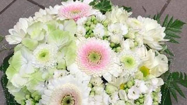 En vakker bukett med hvite og lyserosa blomster, inkludert gerbera og andre blomster, på en grå bakgrunn.