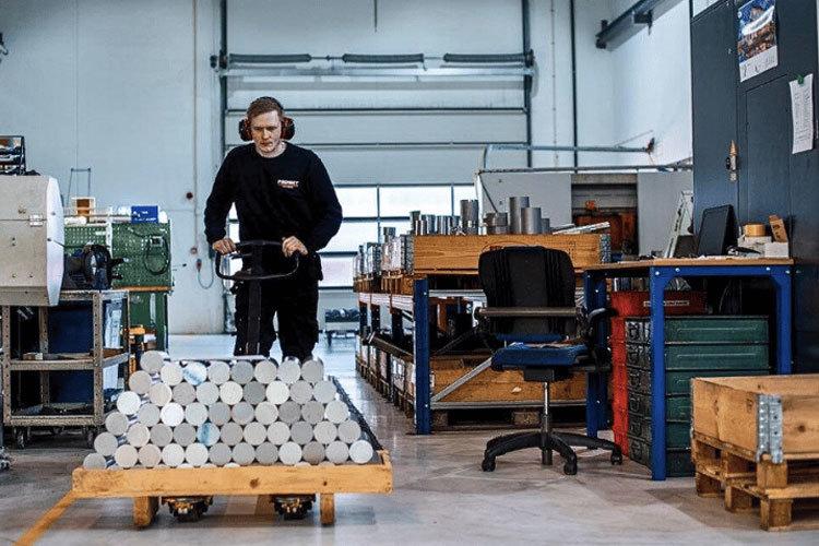 En arbeidstaker bruker en palletrucker til å transportere metallstenger i en moderne fabrikk.