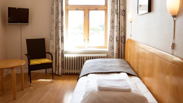 Lys og moderne enkeltrom med en seng, stol, bord og vindu med utsikt.