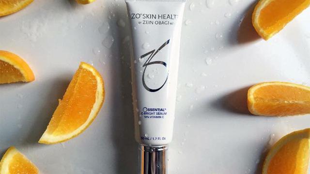 Kremtube fra ZO Skin Health med appelsinskiver rundt, plassert på en fuktig overflate.