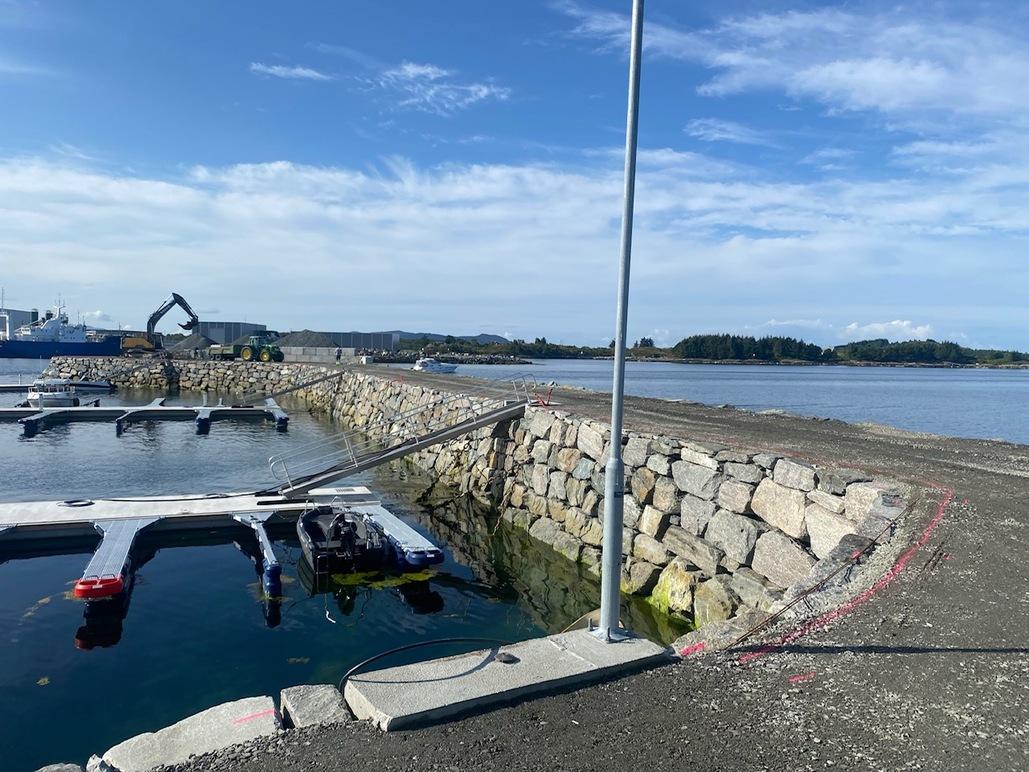 Bilde av en havn med båtplasser, steinmur og en klar blå himmel i bakgrunnen.