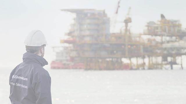 En arbeidstaker i hjelm ser mot en offshore oljeplattform i horisonten.