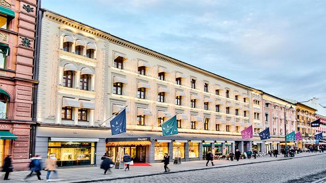 En bygning med flere etasjer og butikker, beliggende på en gate med folk som går forbi.