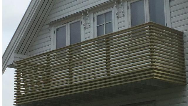 Balkong i tre med horisontale planker på en grå husvegg.