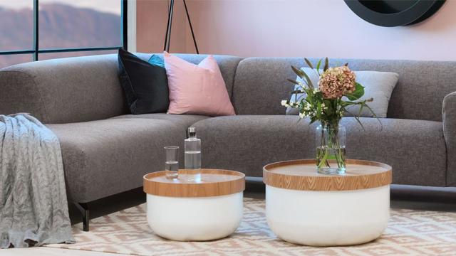 Moderne stue med grå sofa, to runde bord med trelokk, og en vase med blomster på et teppe.