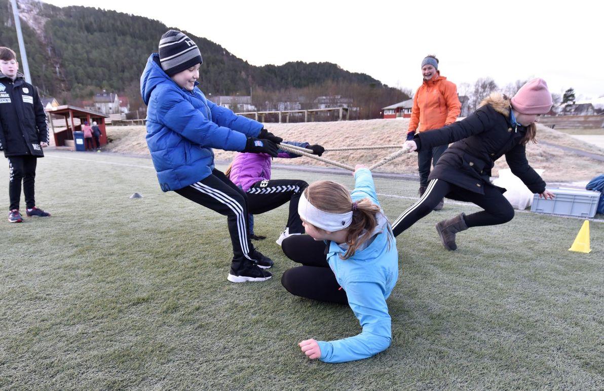 Barn som deltar i en taukrevende konkurranse på en gressbane, med flere deltakere i aktivitet.