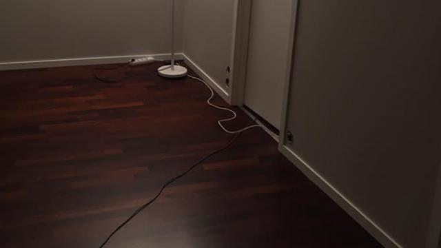 Rom med mørkt tregulv, en lampe med ledning og en dør i bakgrunnen.
