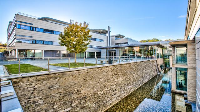 Moderne kontorbygg med glassfasader, grønt område og vannkanal i forgrunnen.