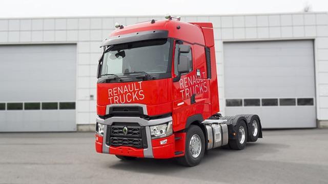 Rød Renault lastebil med påskrift "Renault Trucks" parkert foran en lagerbygning.