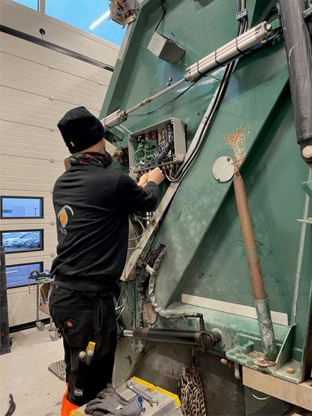 En tekniker jobber med elektriske komponenter på en stor maskin i et verksted.