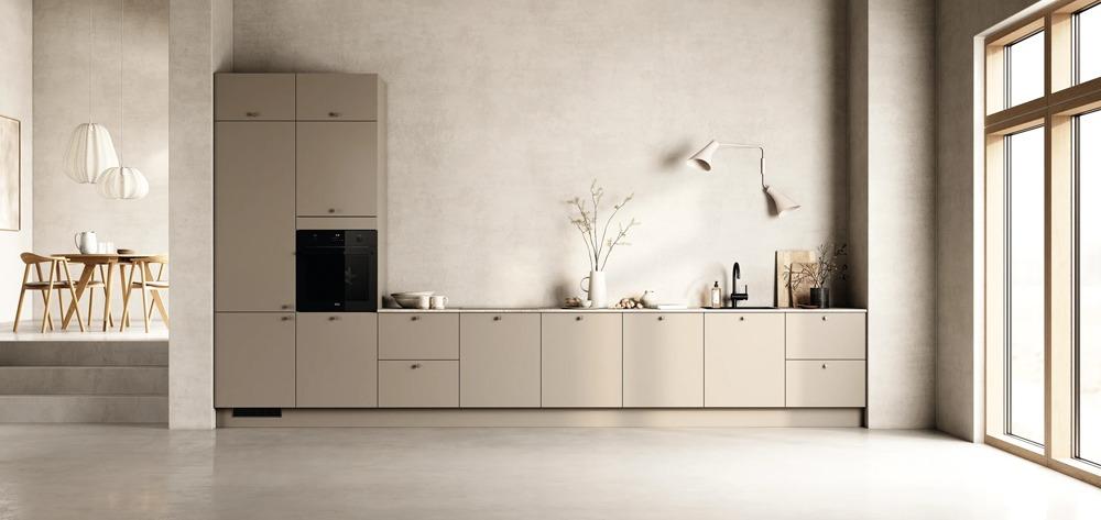 Moderne kjøkkeninnredning med beige skap, hvite vegger og store vinduer som slipper inn naturlig lys.