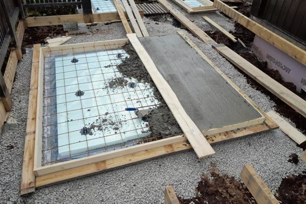 Bilde av en byggeplass med en nylig støpt betongplate omgitt av treplanker og grus.