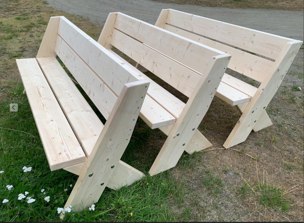 Tre benker laget av lys tre, plassert på gresset i et utendørsområde.