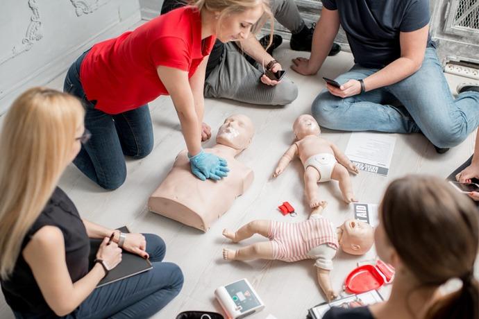 En gruppe mennesker deltar i førstehjelpskurs med hjerte-lunge-redning på dukker og en babydukke.