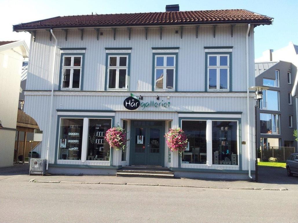 En sjarmerende frisørsalong med blomsterkasser foran, beliggende i en hvit bygning med flere vinduer.