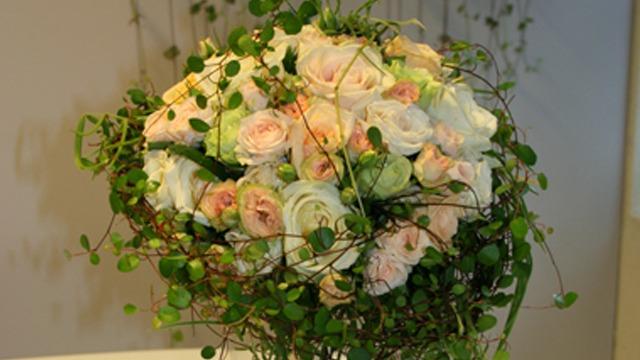 En vakker bukett med rosa og hvite roser, dekorert med grønne blader og slyngplanter.